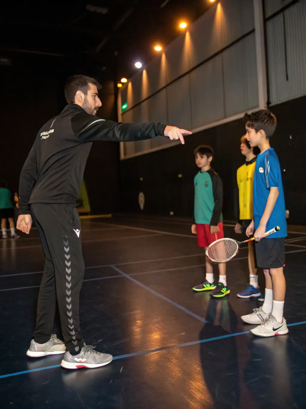 An image of a coach instructing a group of serious players during a training session on a professional badminton court, showcasing the competitive training programs.